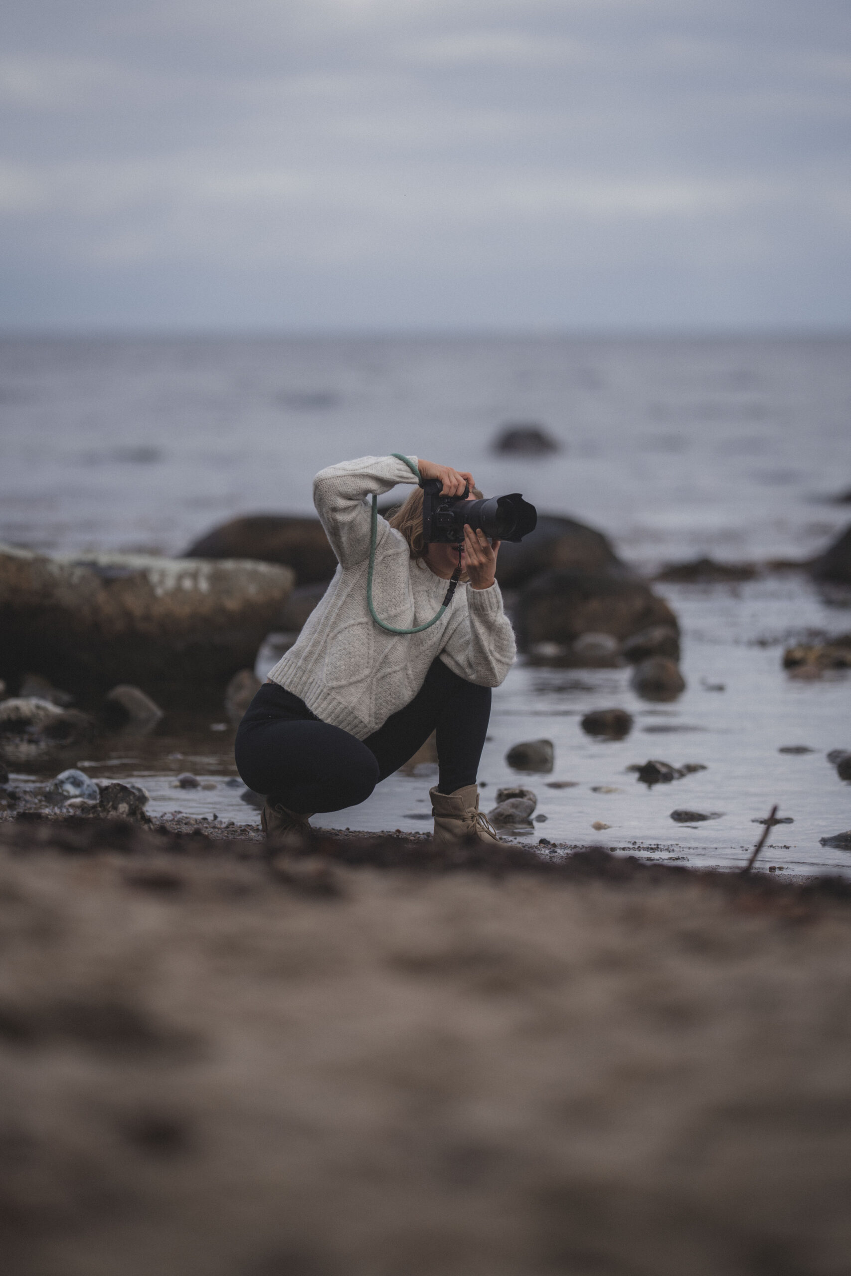 Fotografin hockt am Strand und fotografiert mit Profi-Kamera
