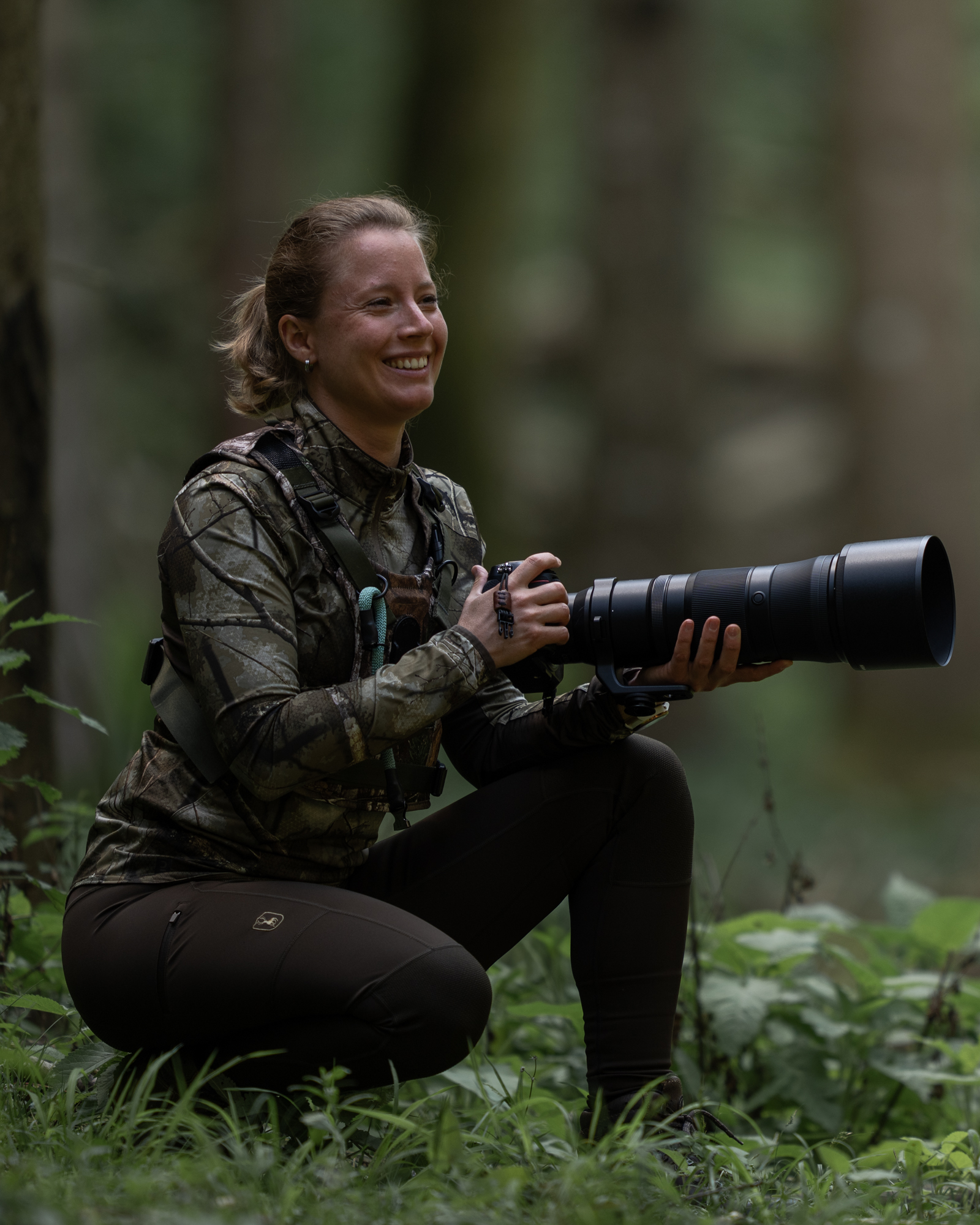 Fotografin lächelt im Wald mit Teleobjektiv in der Hand